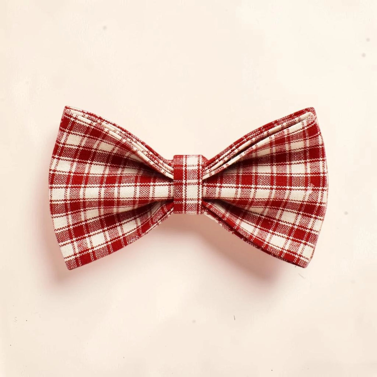 A red and white plaid dog bow tie made of woven fabric.