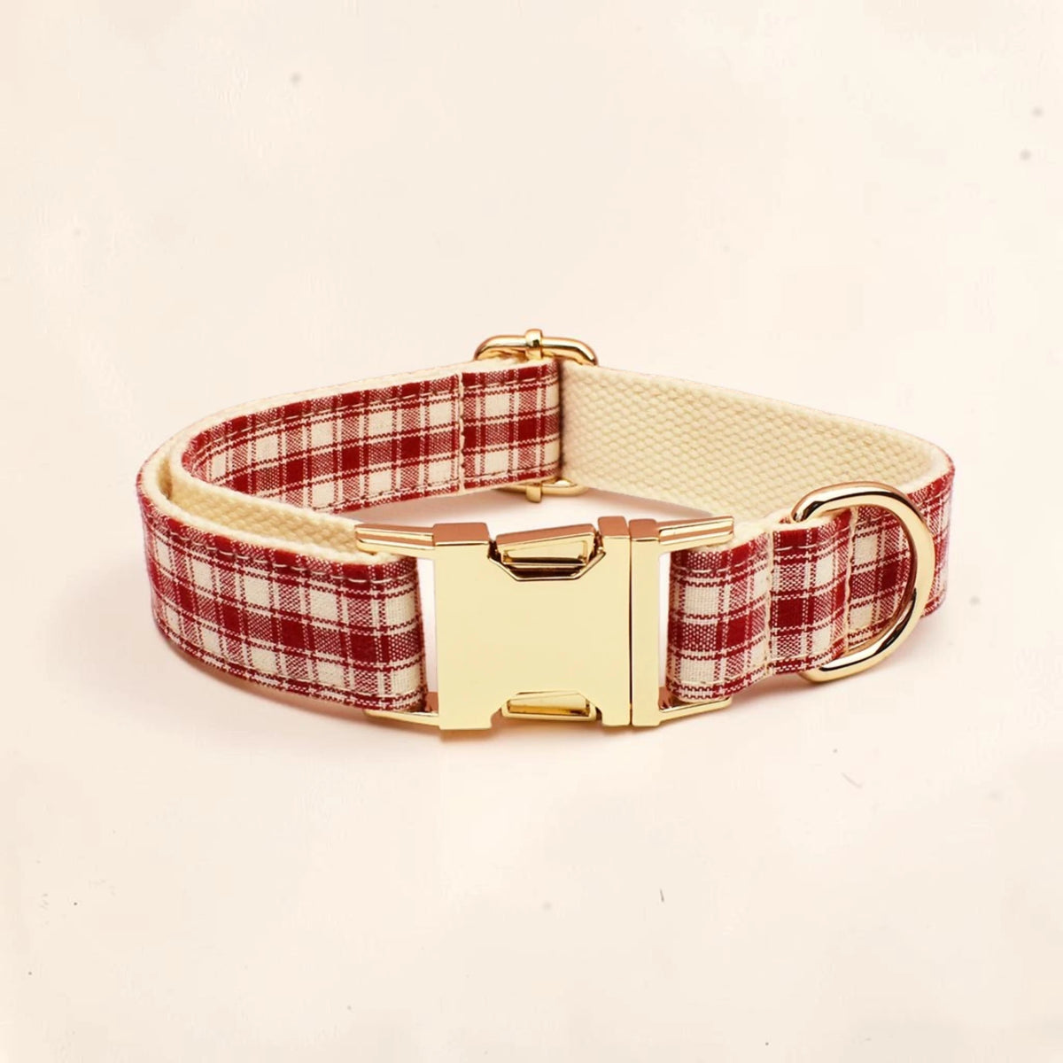 A dog collar with a red and white plaid pattern, a cream-colored inner lining, and a shiny gold-tone buckle and D-ring.