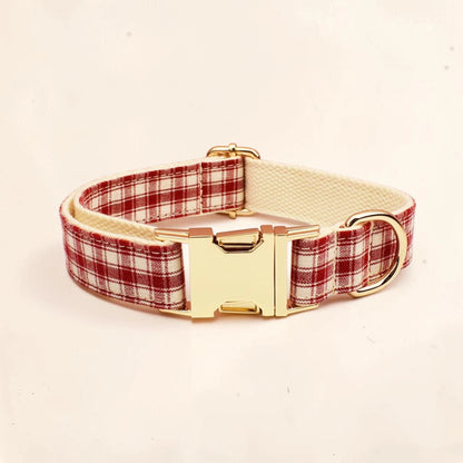 A dog collar with a red and white plaid pattern, a cream-colored inner lining, and a shiny gold-tone buckle and D-ring.
