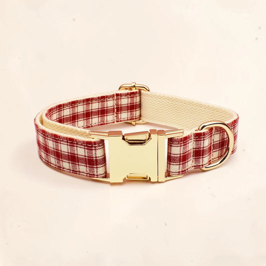 A dog collar with a red and white plaid pattern, a cream-colored inner lining, and a shiny gold-tone buckle and D-ring.
