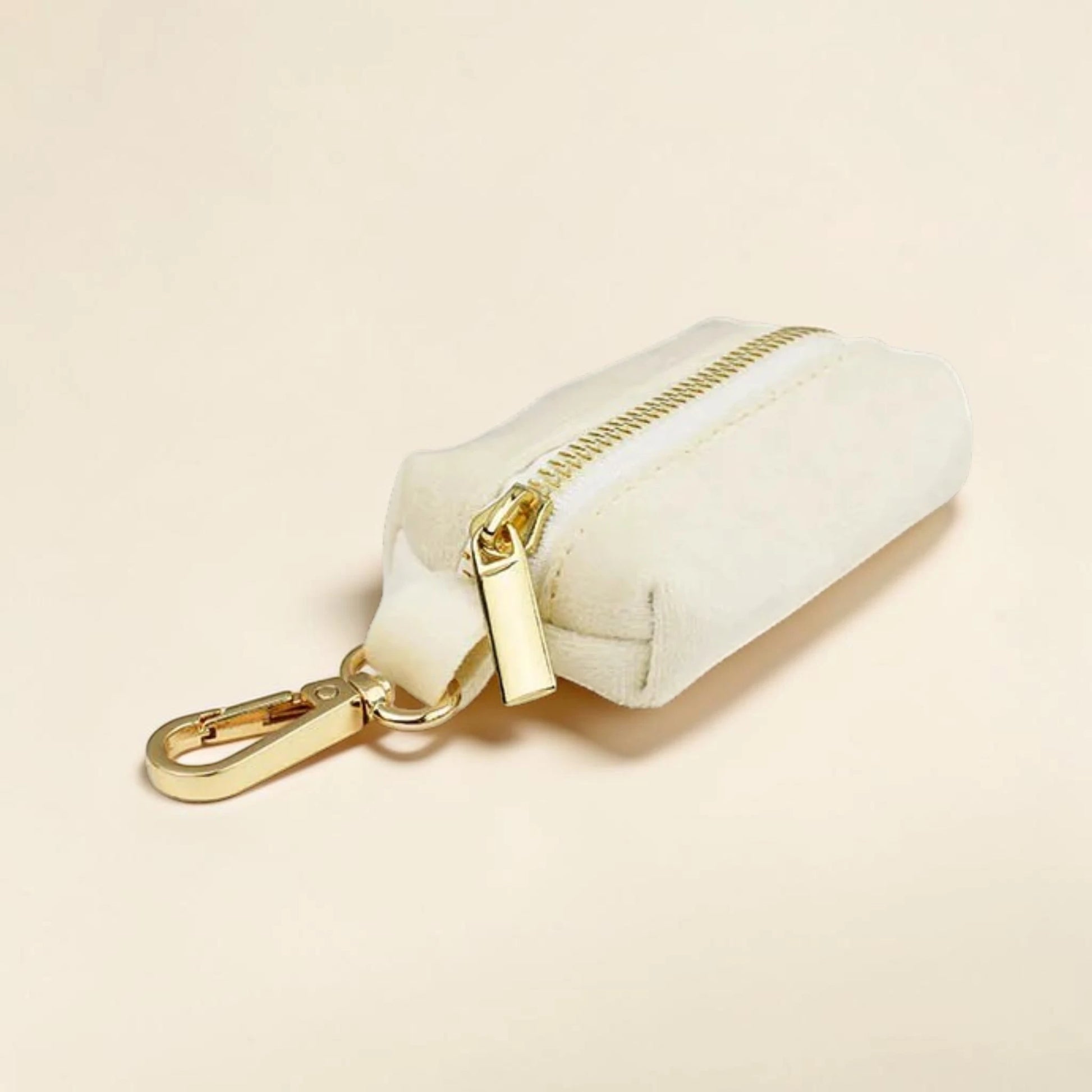Ivory dog poop bag holder with a gold zip and clip on a beige background
