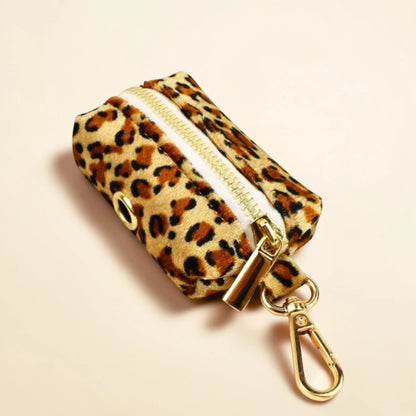 Leopard print dog poop bag holder with gold zip and clip on a beige background