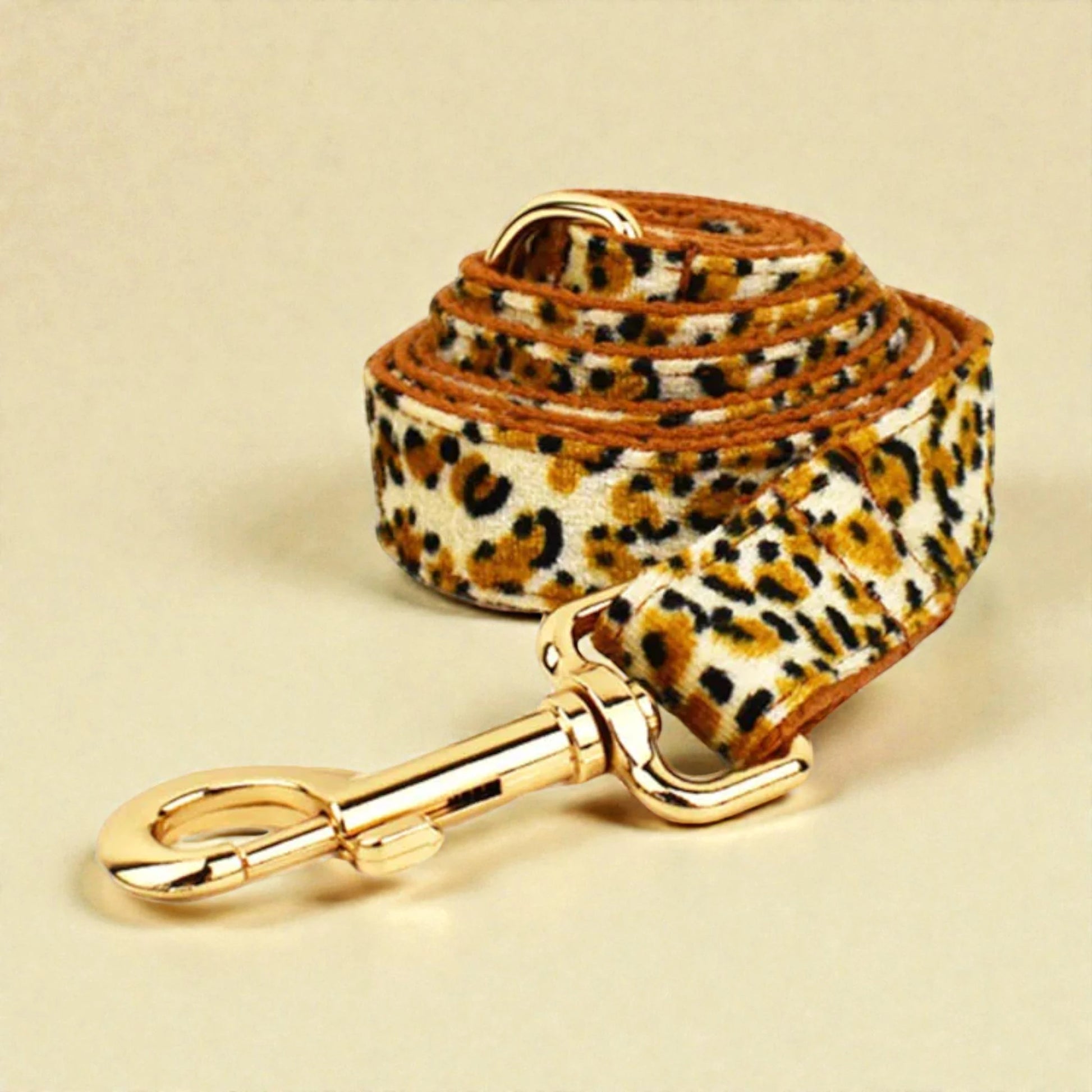 Leopard print dog lead with gold clip on a beige background