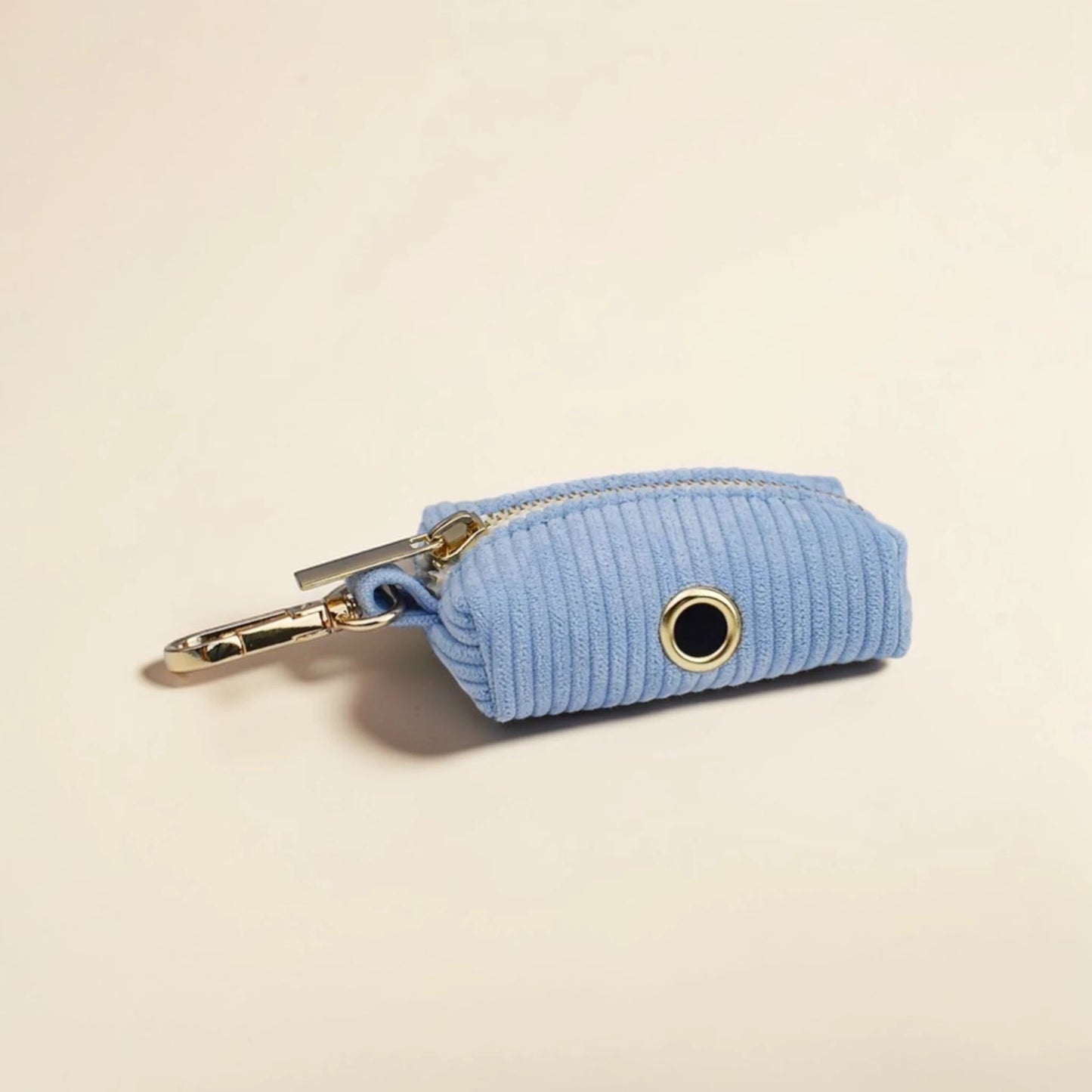 Light blue corduroy dog poop bag holder with gold zip on a beige background