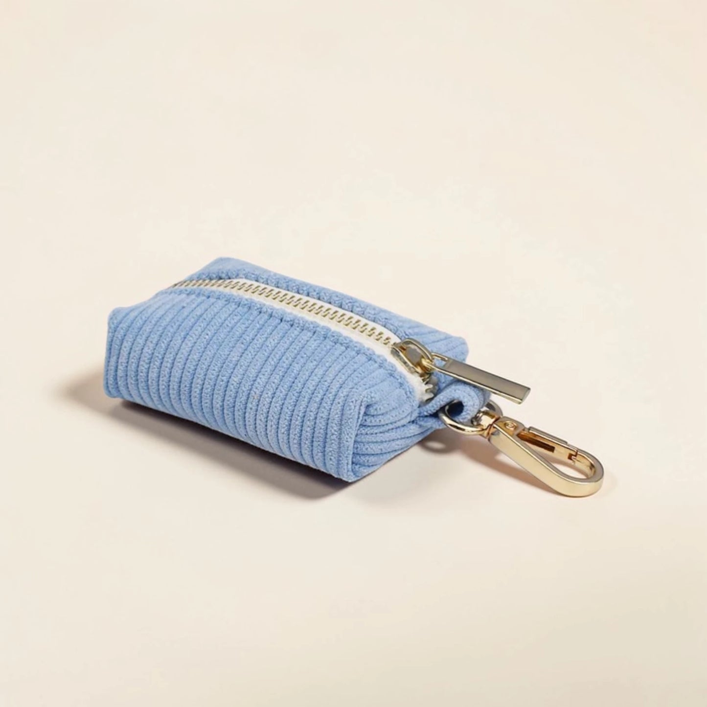 Light blue corduroy dog poop bag holder with a gold zip and clip on a beige background