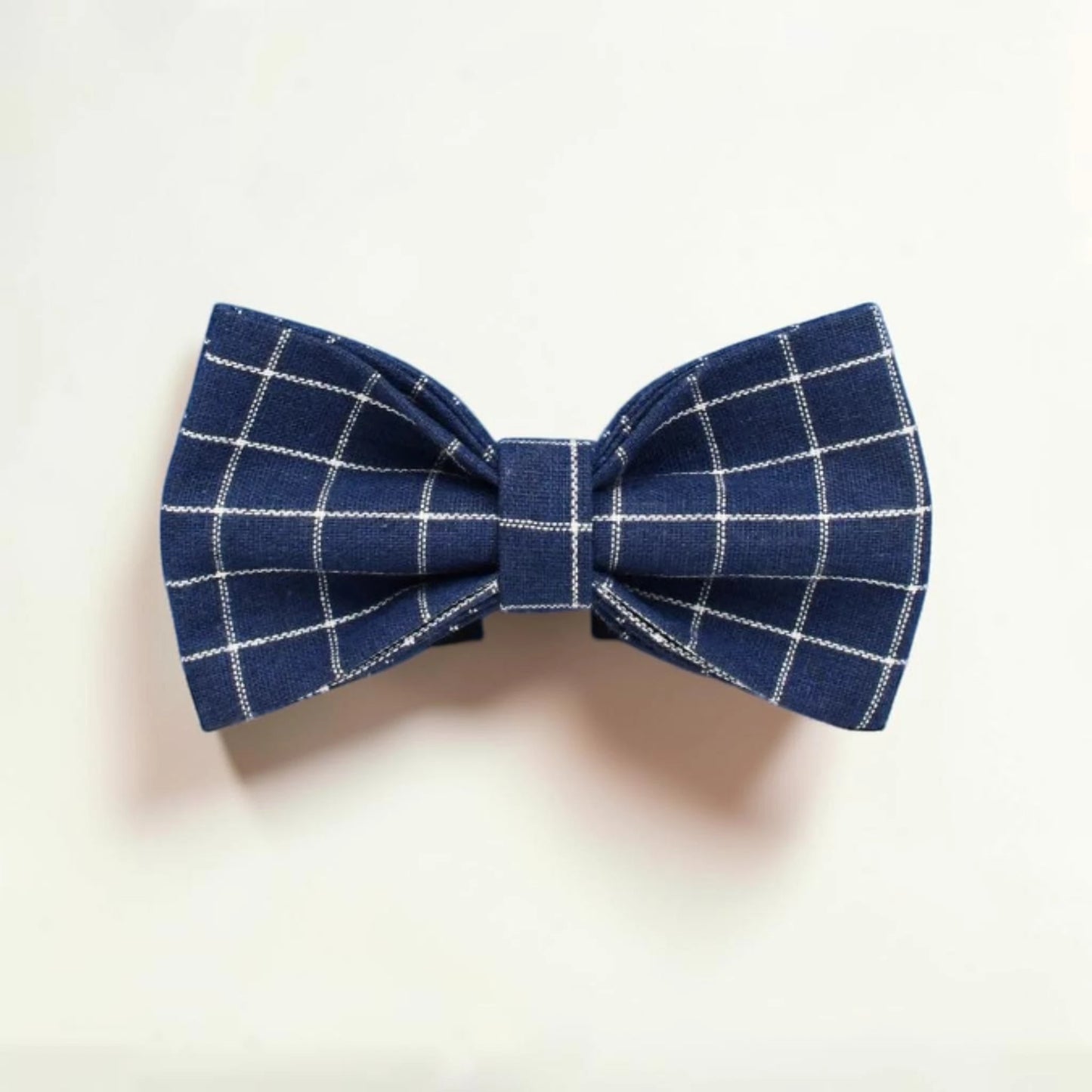 Blue check dog bow tie on a light beige background
