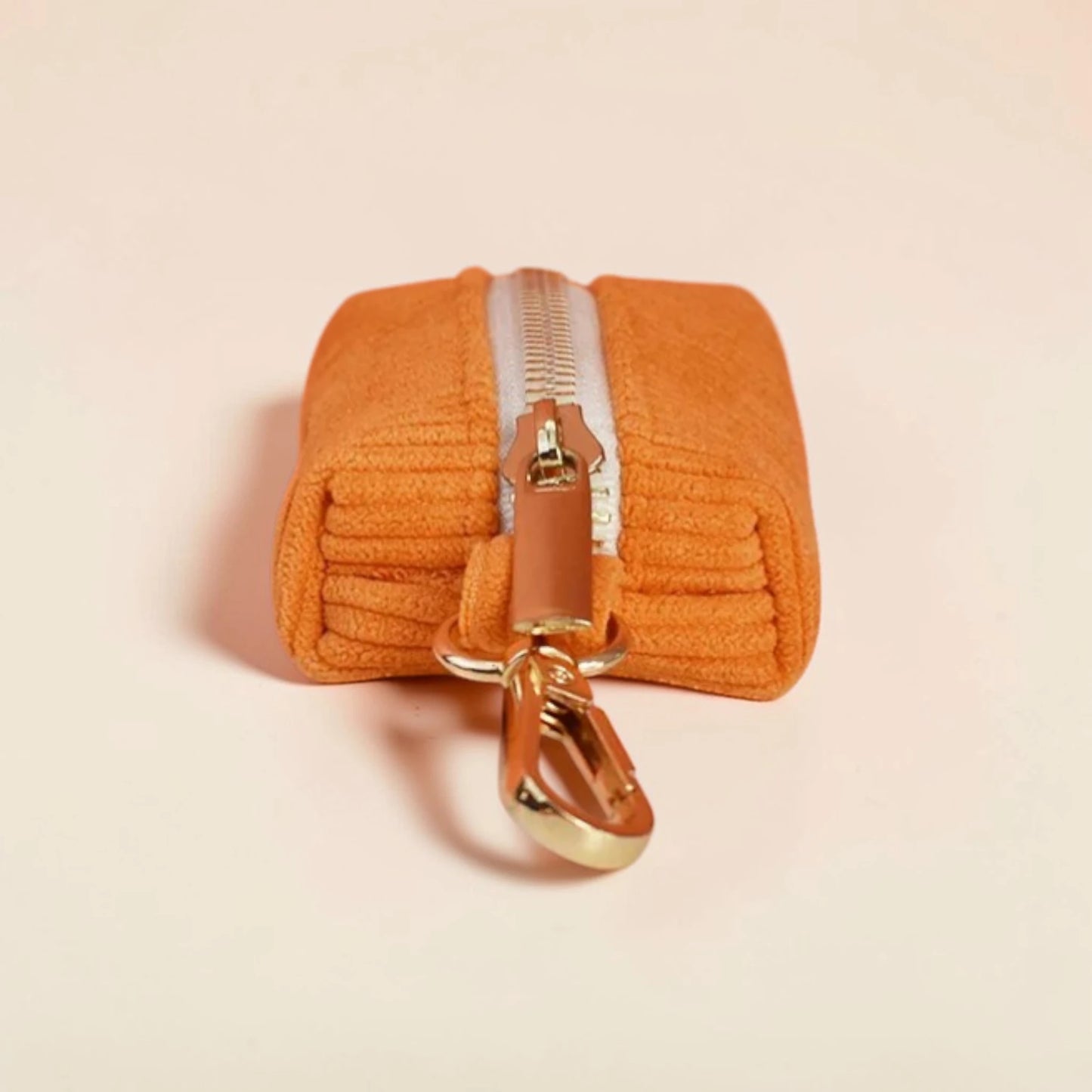 Orange dog poop bag holder with a gold zip on a beige background