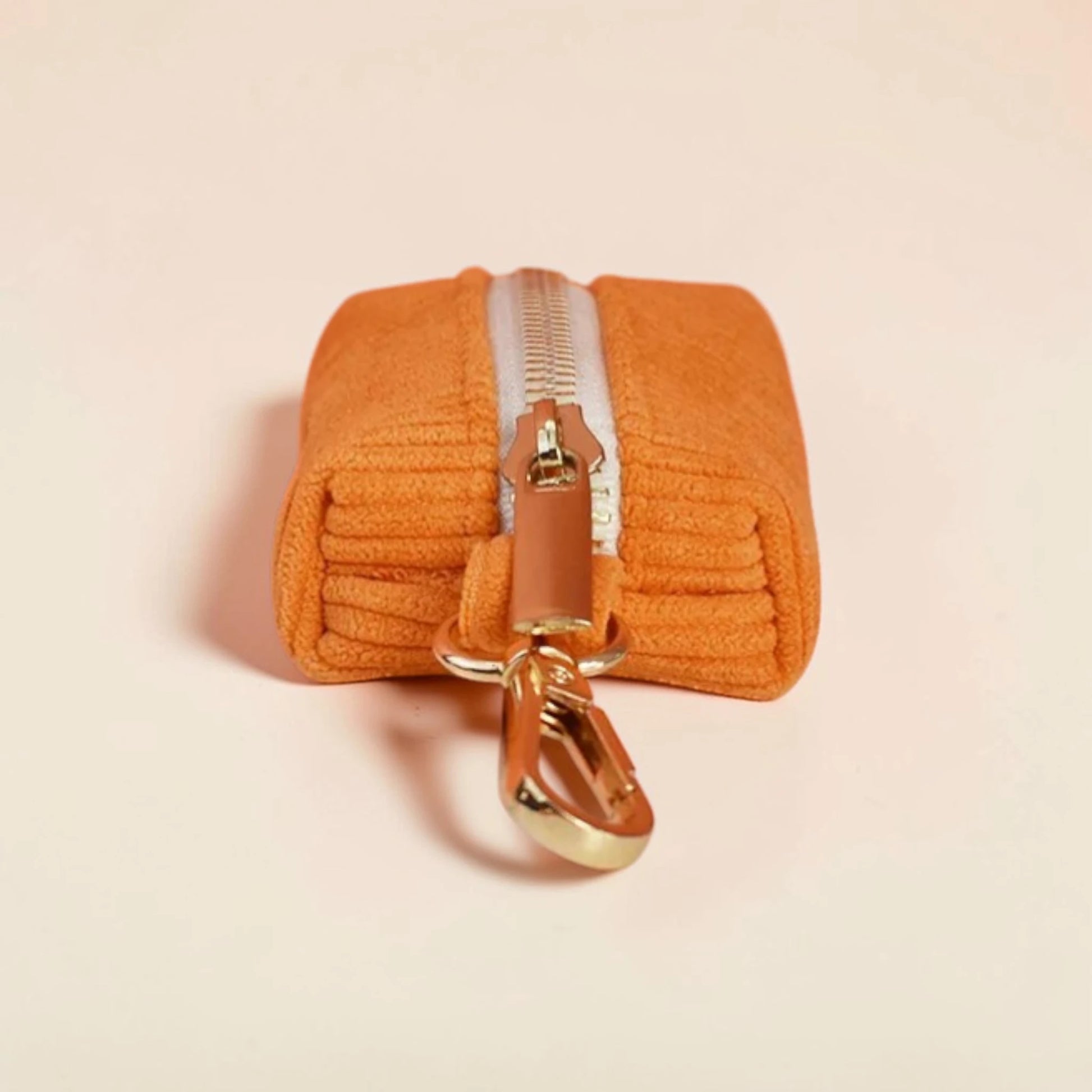 Orange dog poop bag holder with a gold zip on a beige background