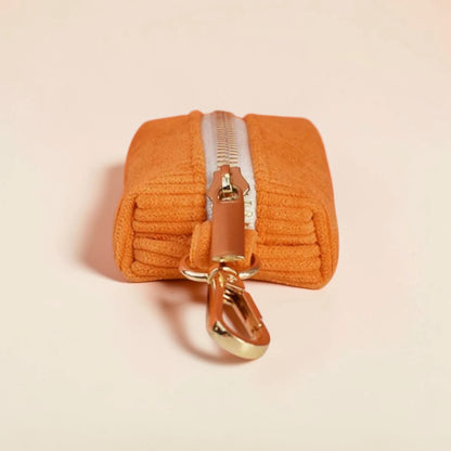 Orange dog poop bag holder with a gold zip on a beige background