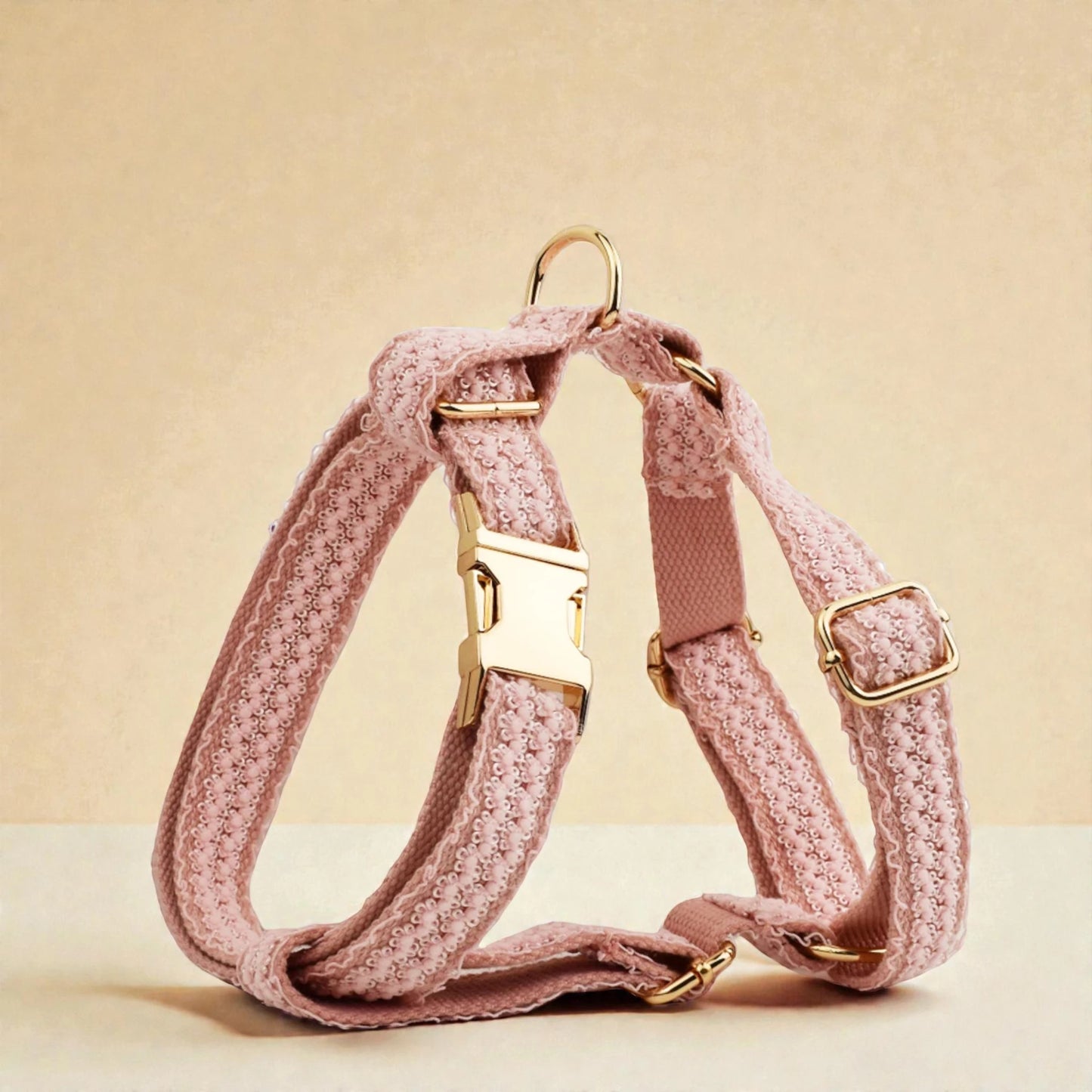 Pink dog harness with gold hardware on a beige background