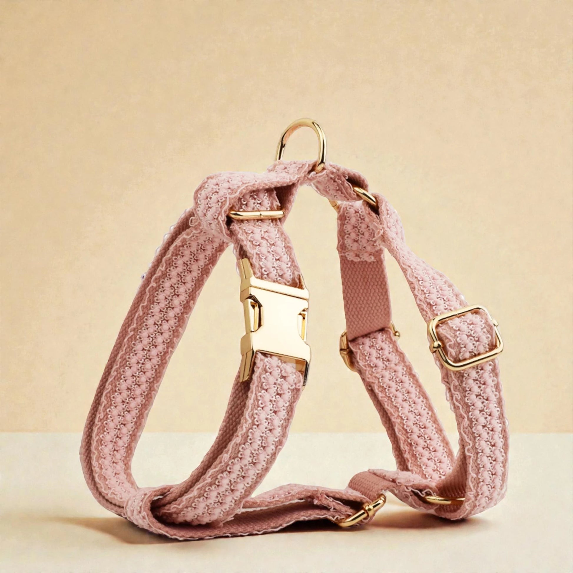 Pink dog harness with gold hardware on a beige background