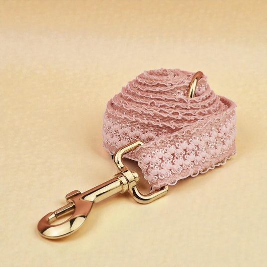 Pink lace dog lead with gold hardware on a beige background