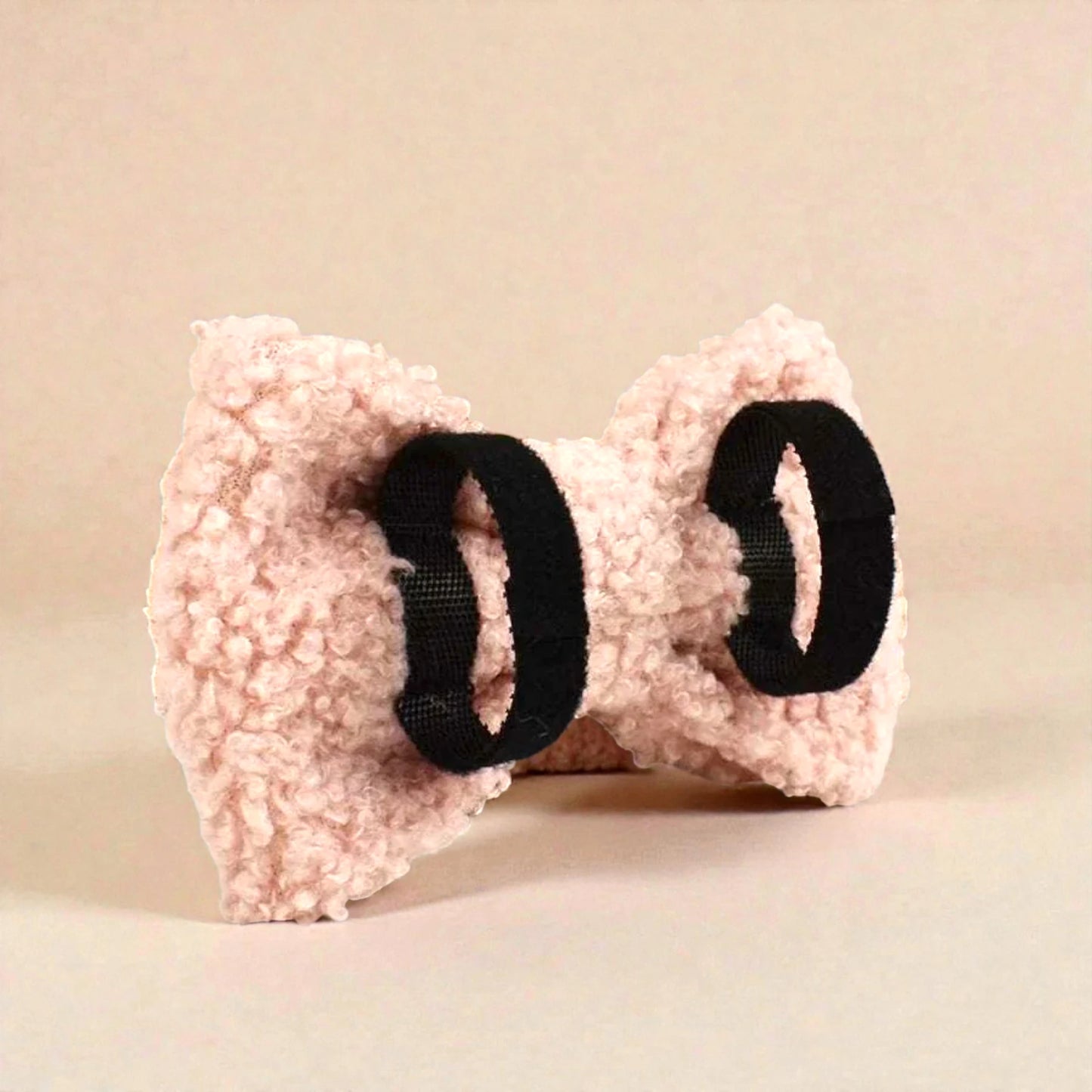 Pink fleece bow with black elastic on a beige background