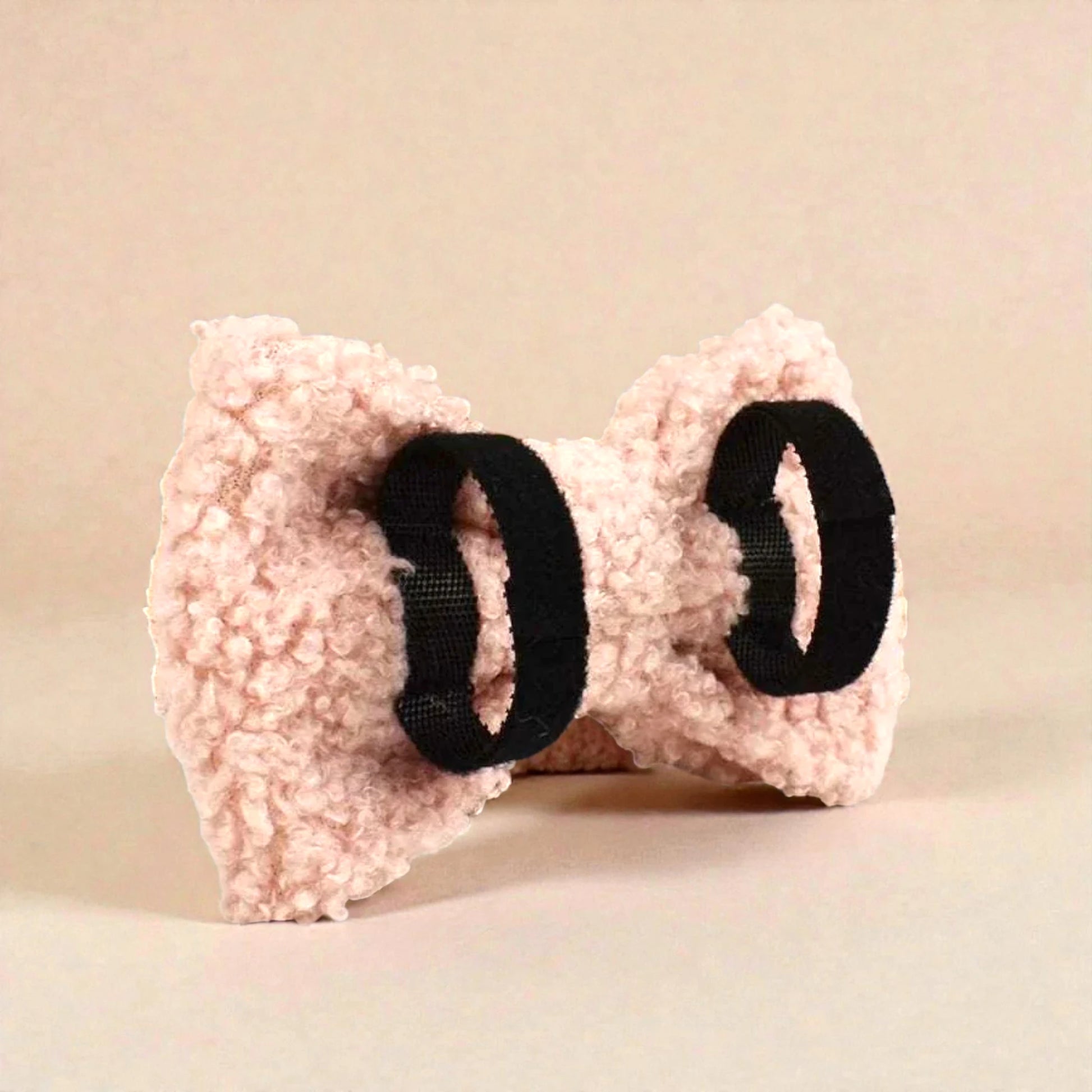 Pink fleece bow with black elastic on a beige background