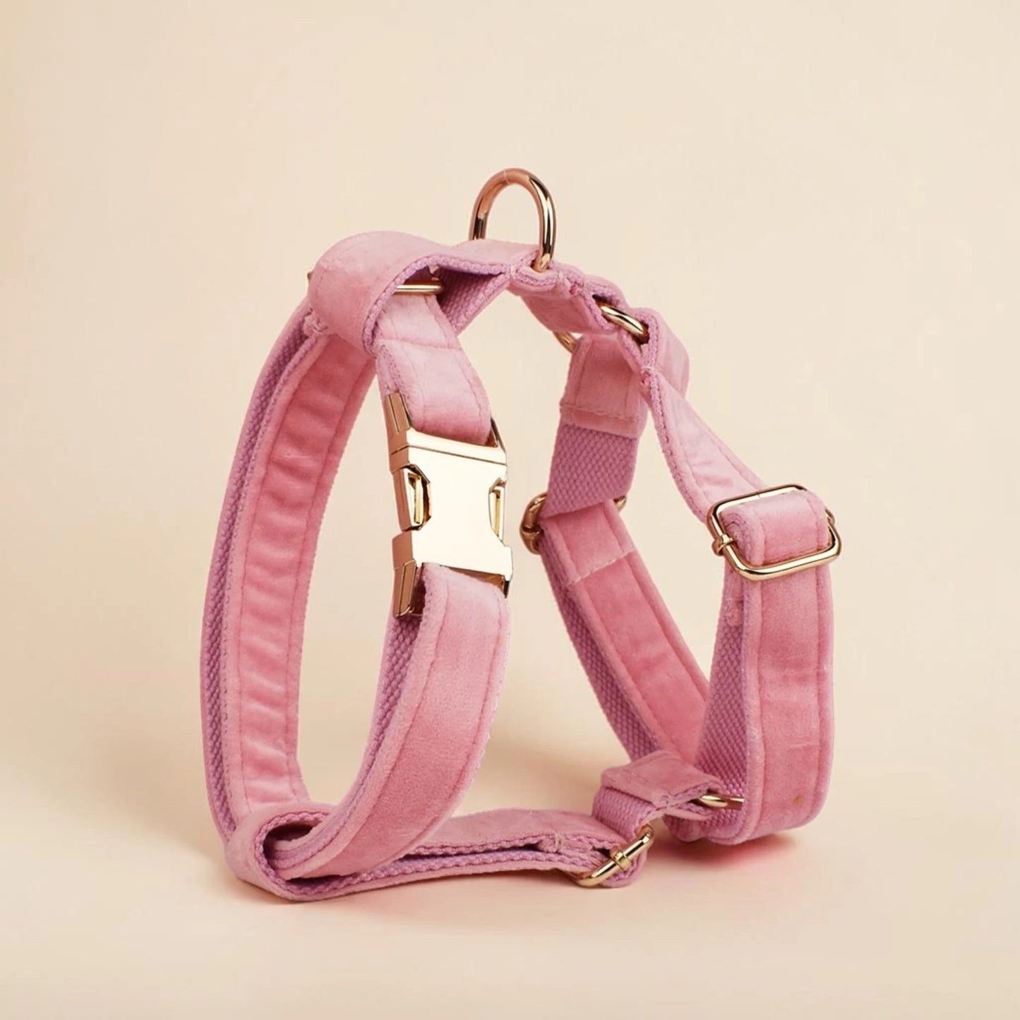 Pink dog harness with gold hardware on a beige background