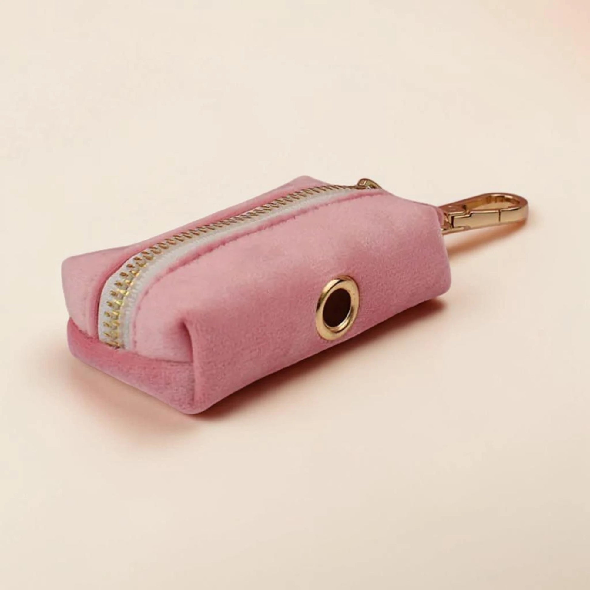 Pink dog poop bag holder with gold zip and clip on a beige background