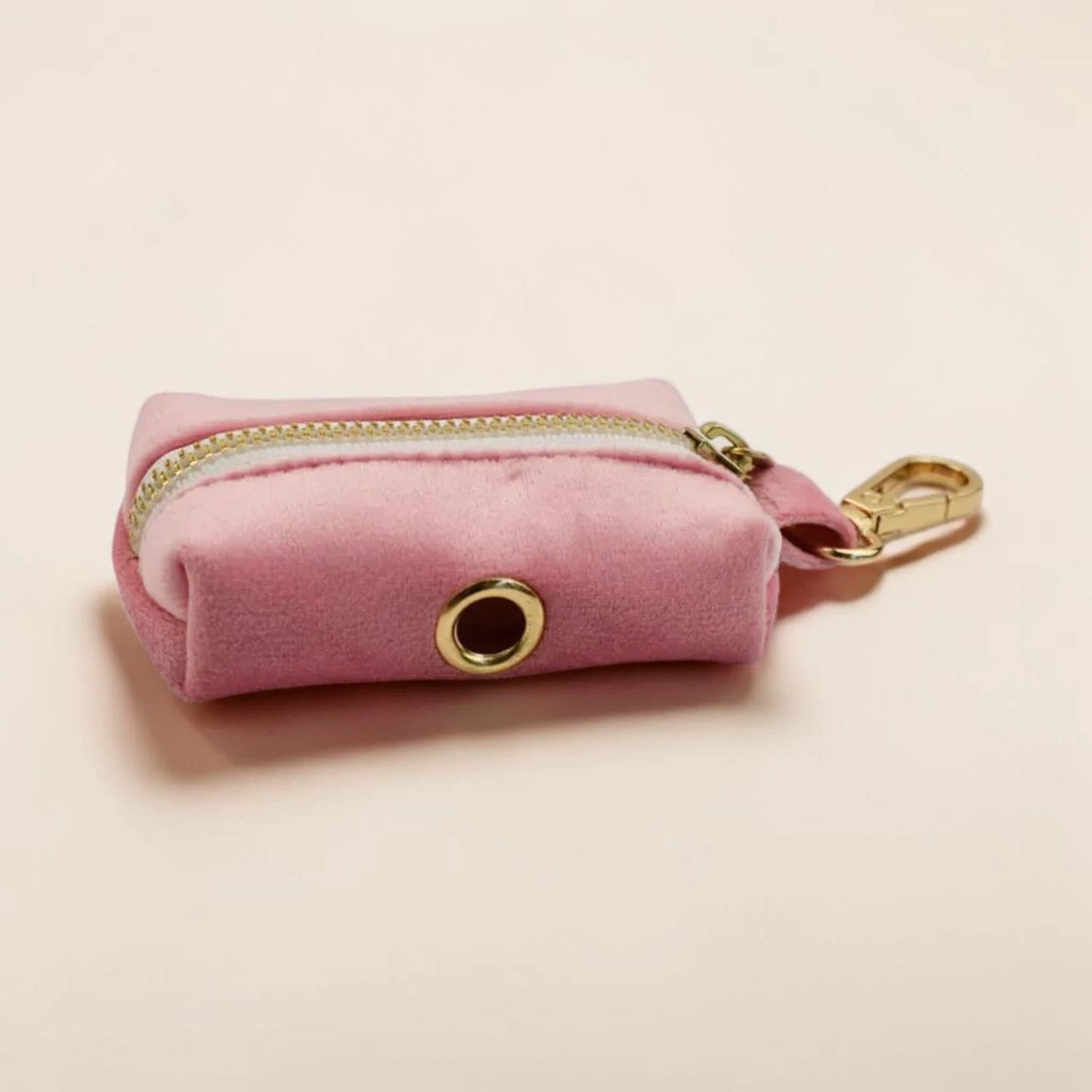 Pink velvet dog poop bag holder with gold zip and clip on a beige background