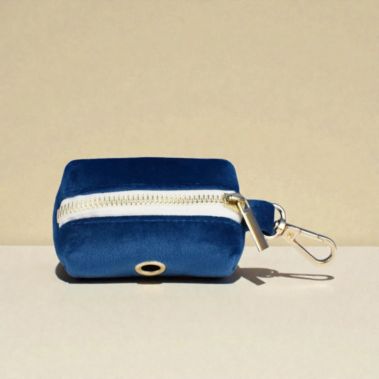 Blue velvet dog poop bag holder with gold zipper and clasp on a beige background
