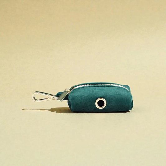 Dark green dog poop bag holder with a gold clip on a beige background