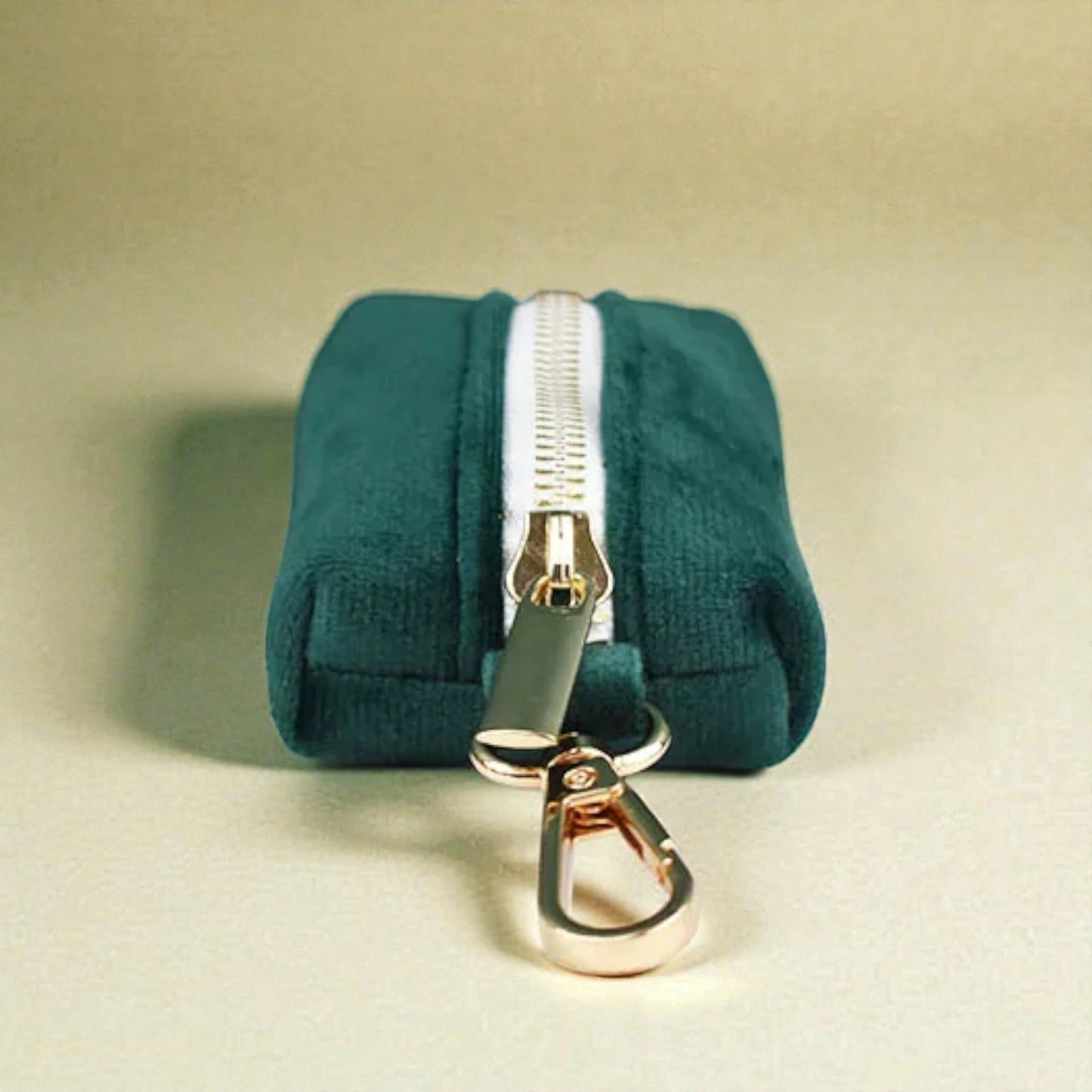 Green dog poop bag holder with a gold zip and clip on a beige background