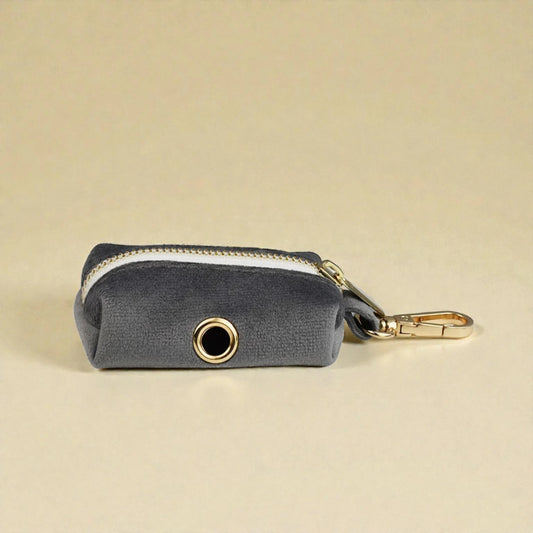 Grey dog poop bag holder with gold zip and clip on a beige background