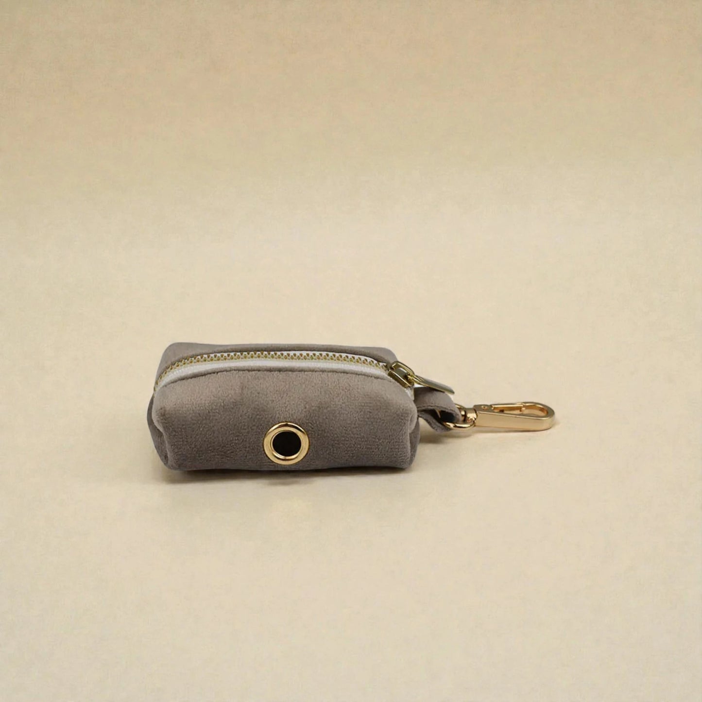 Grey dog poop bag holder with gold zip and clip on a beige background