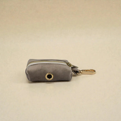 Grey dog poop bag holder with gold zip and clip on a beige background