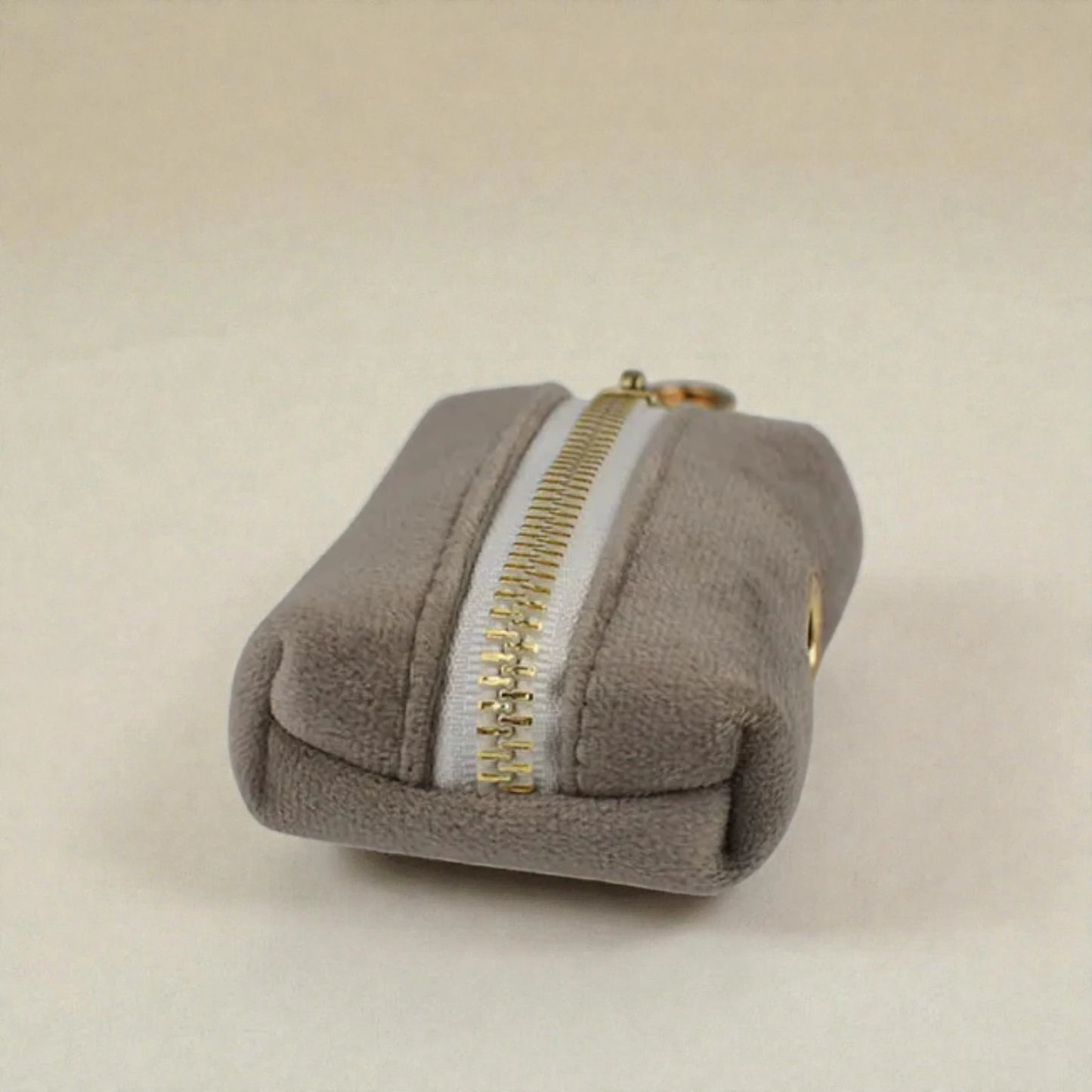 Grey dog poop bag holder with a gold zip on a beige background