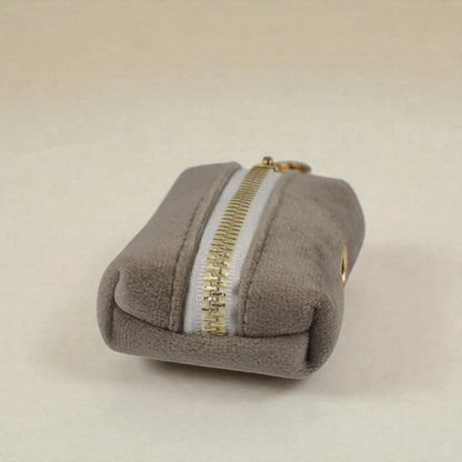Grey dog poop bag holder with a gold zip on a beige background