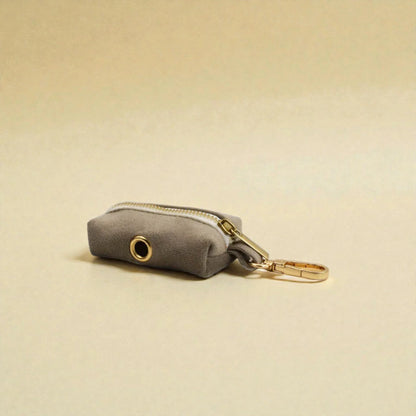 Grey dog poop bag holder with gold zip and clip on a beige background