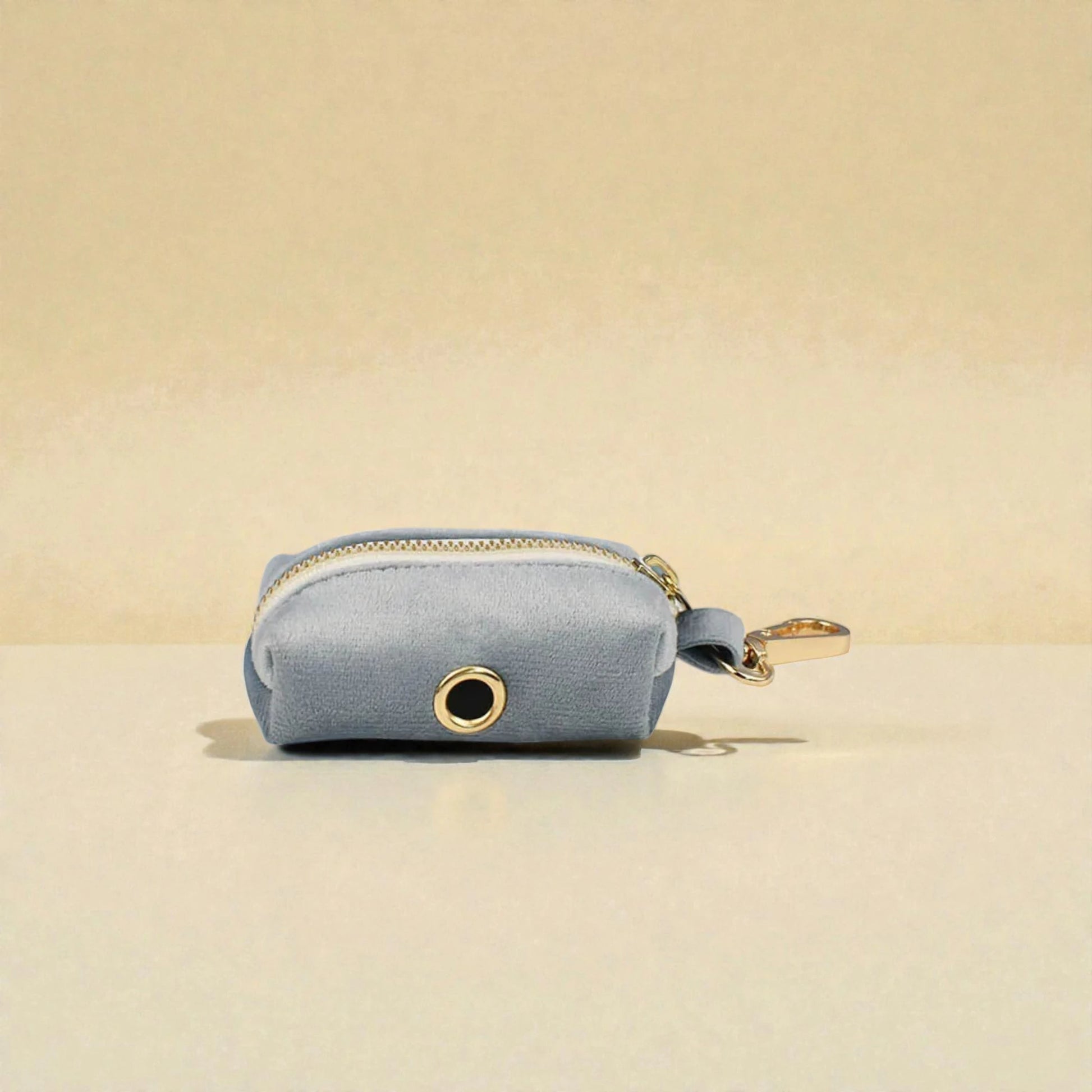 Pale blue dog poop bag holder with a gold zip on a beige background