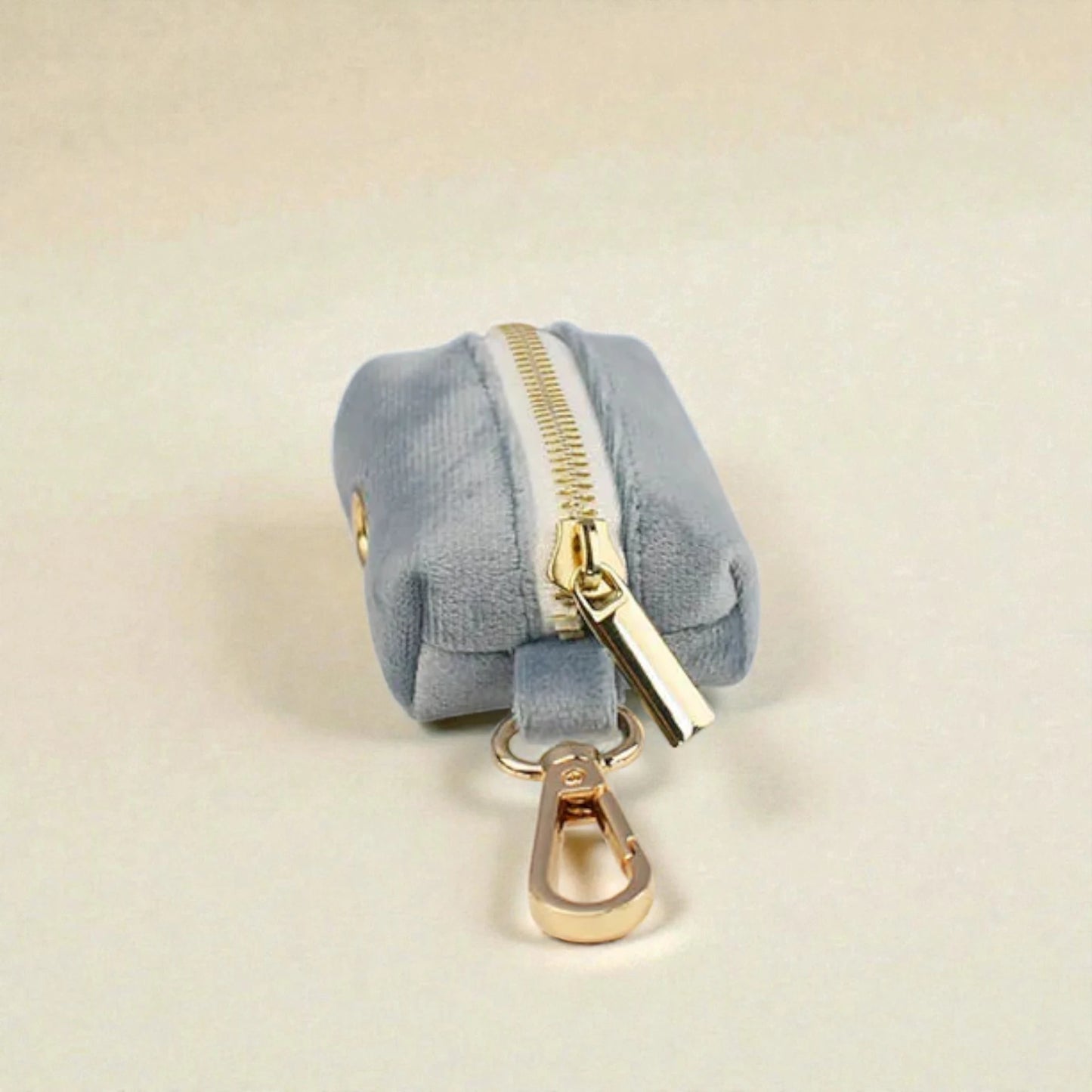 Pale blue dog poop bag holder with gold zip and clip on a beige background