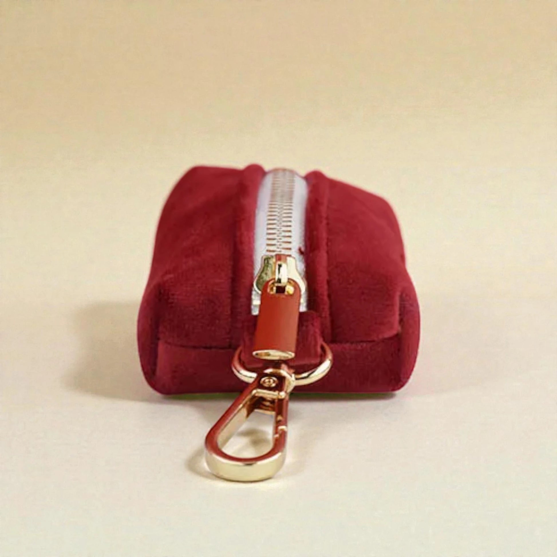 Red dog poop bag holder with a gold zip and clip on a beige background