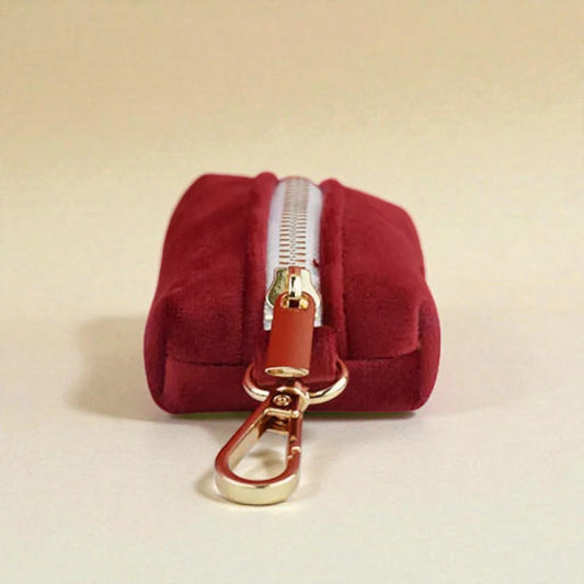 Red dog poop bag holder with a gold zip and clip on a beige background