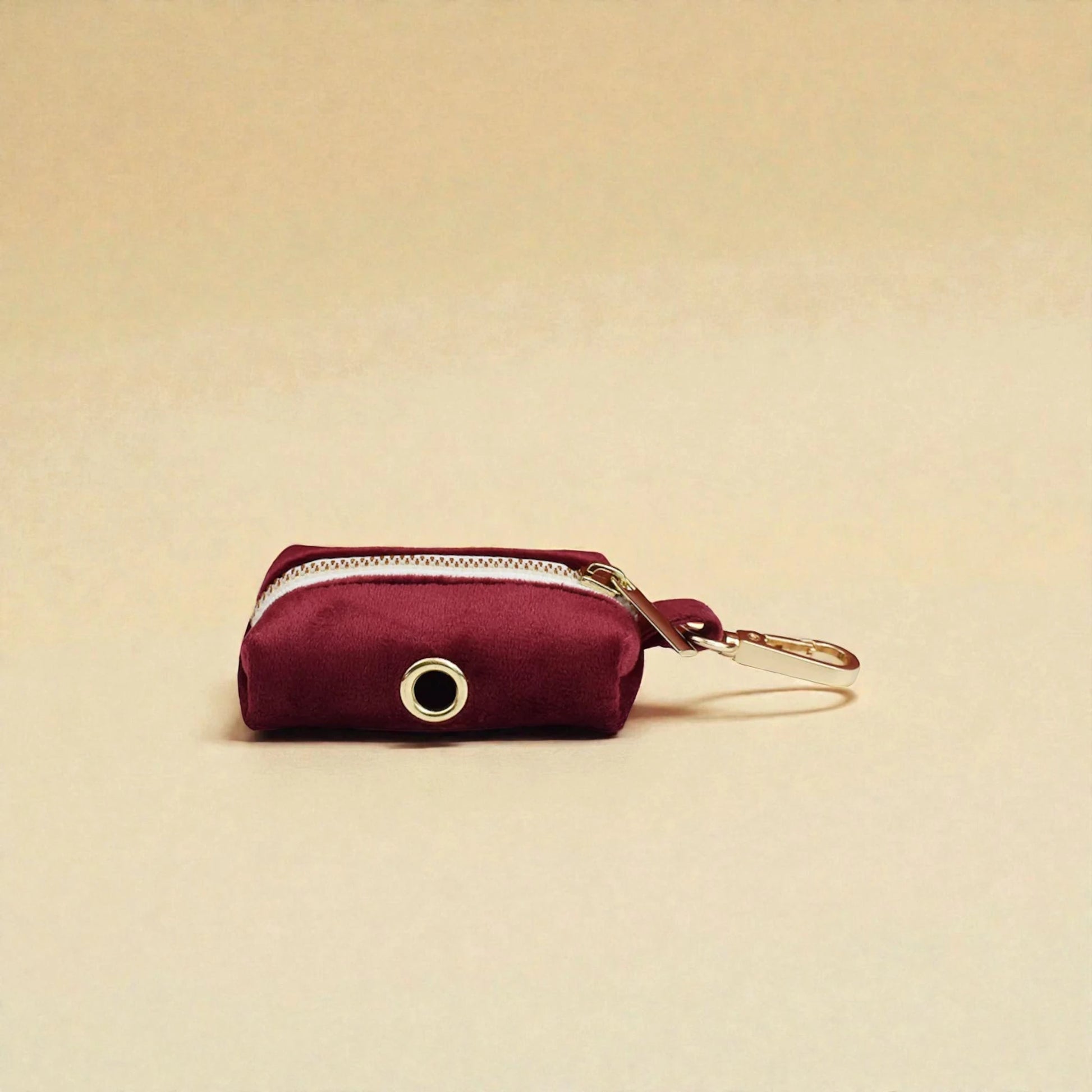 Red wine dog poop bag holder with gold zip and clip on a beige background