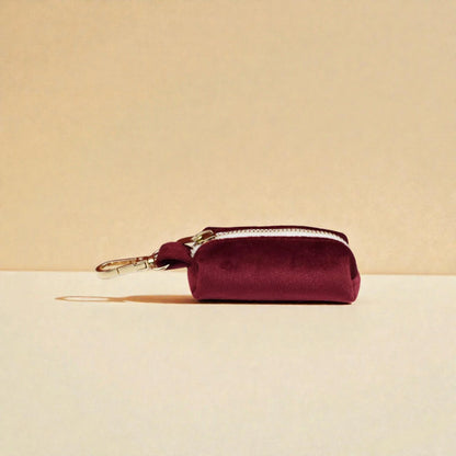 Red wine dog poop bag holder with a gold clip on a beige background