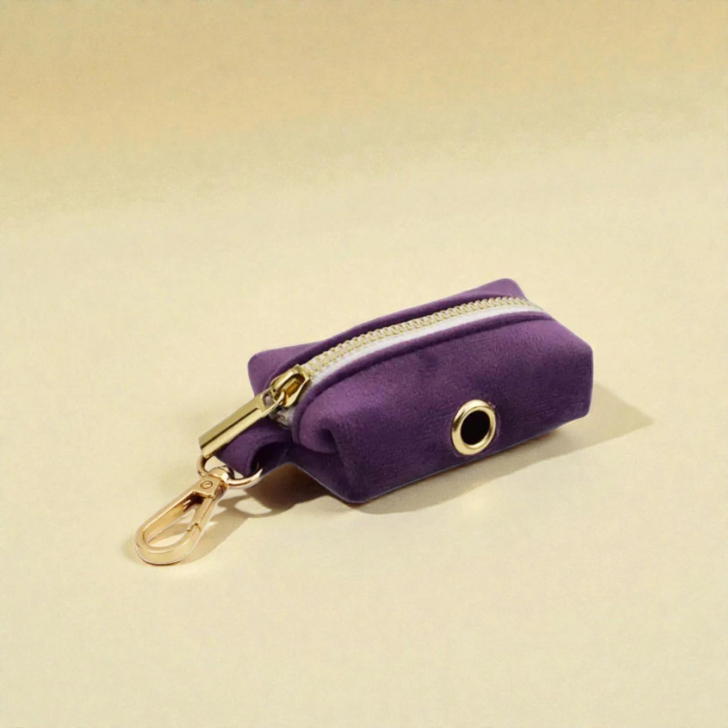 Purple velvet poop bag holder with gold zip and clip on a beige background