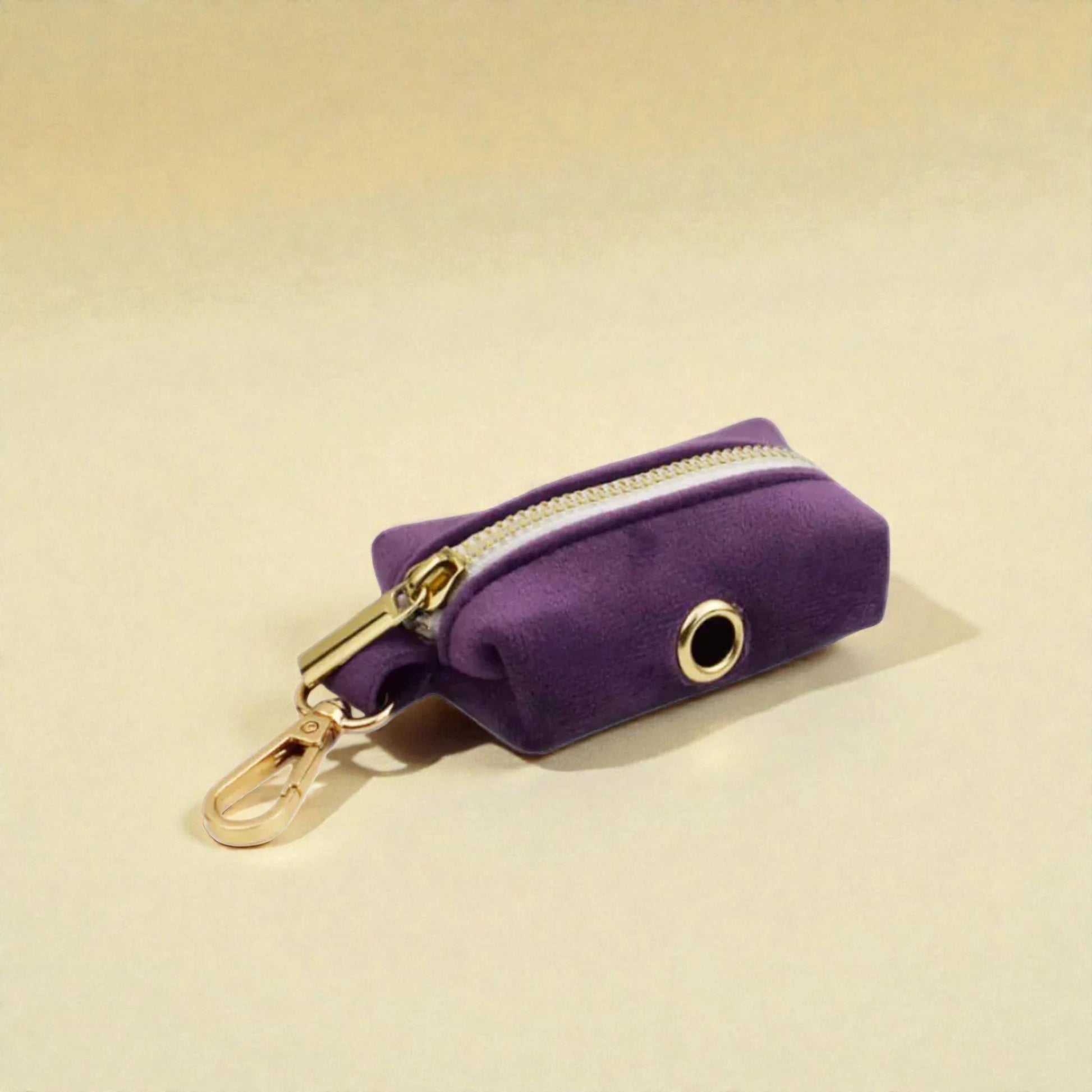 Purple velvet poop bag holder with gold zip and clip on a beige background