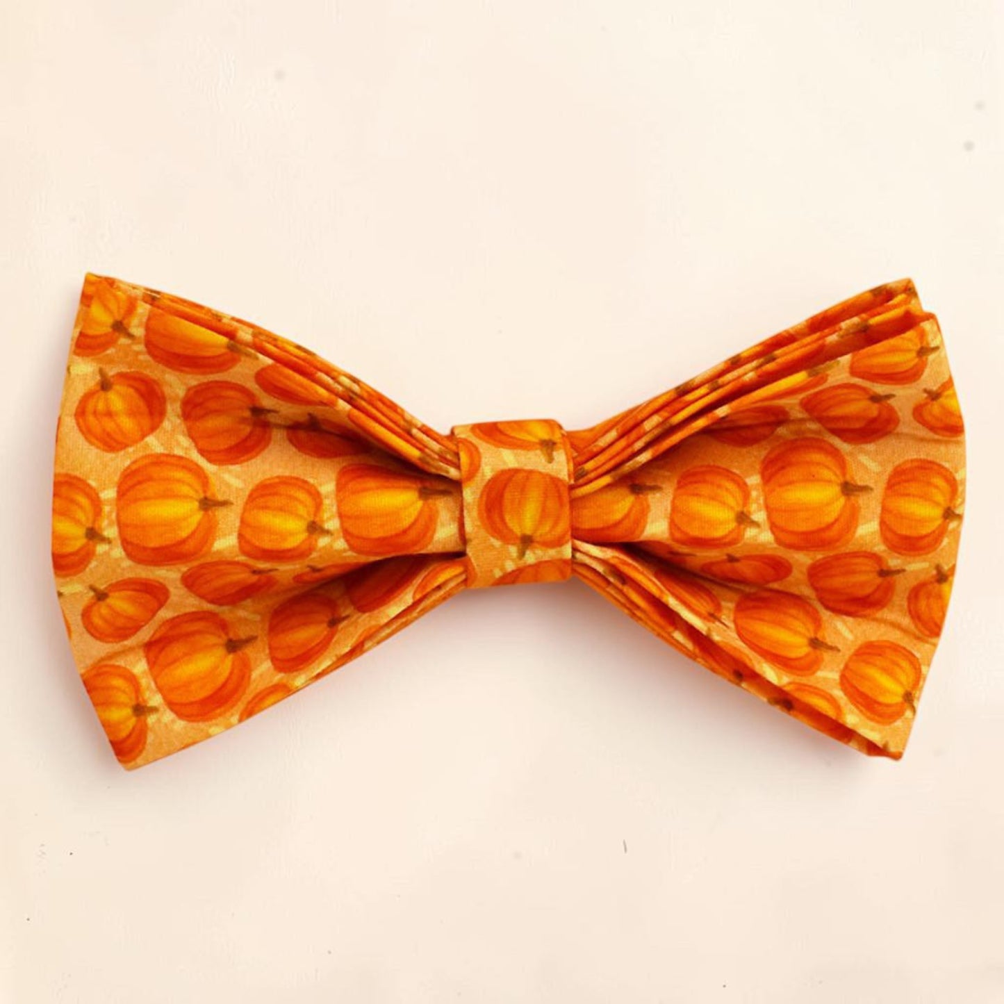 A dog bow tie featuring an all-over pumpkin pattern in shades of orange and yellow.