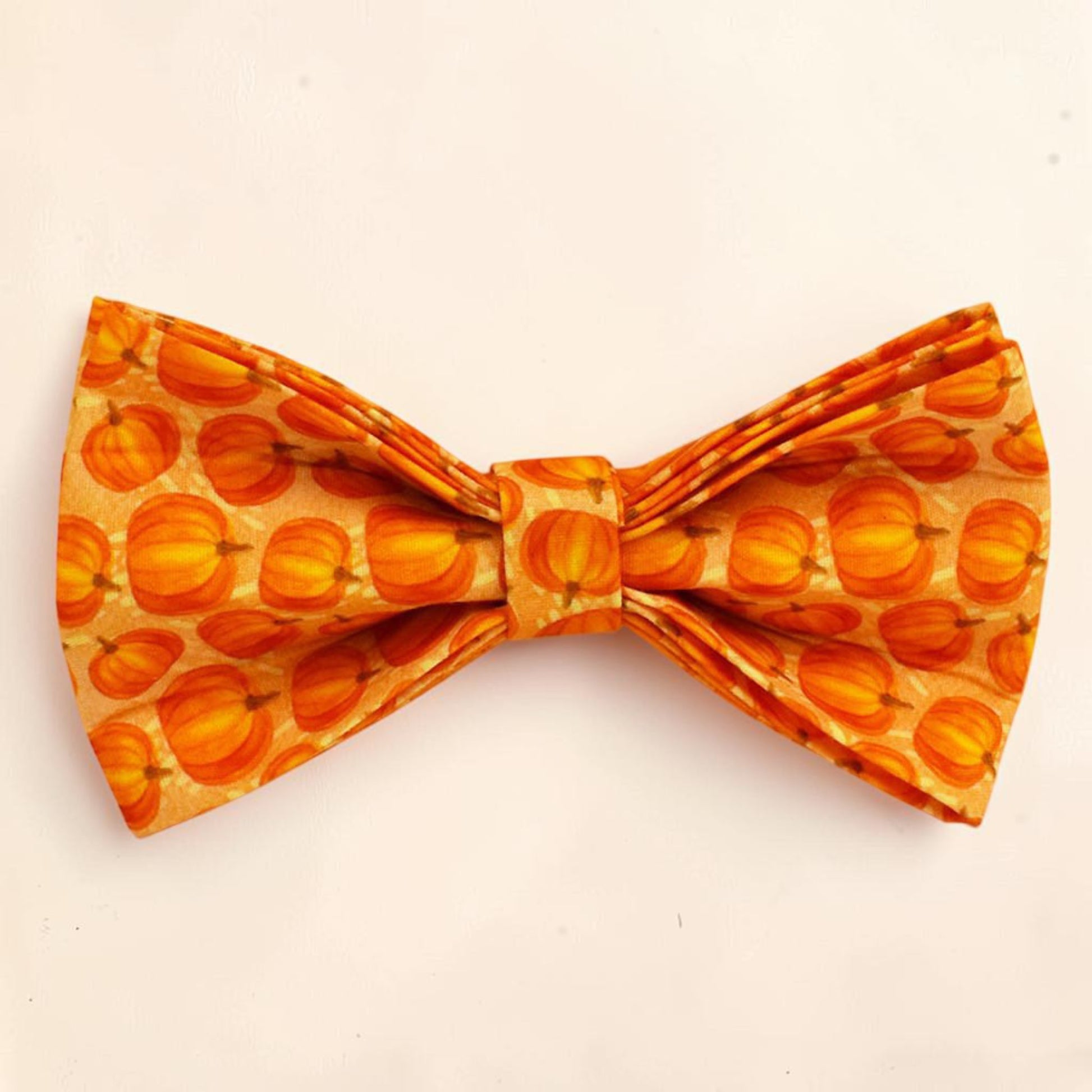 A dog bow tie featuring an all-over pumpkin pattern in shades of orange and yellow.