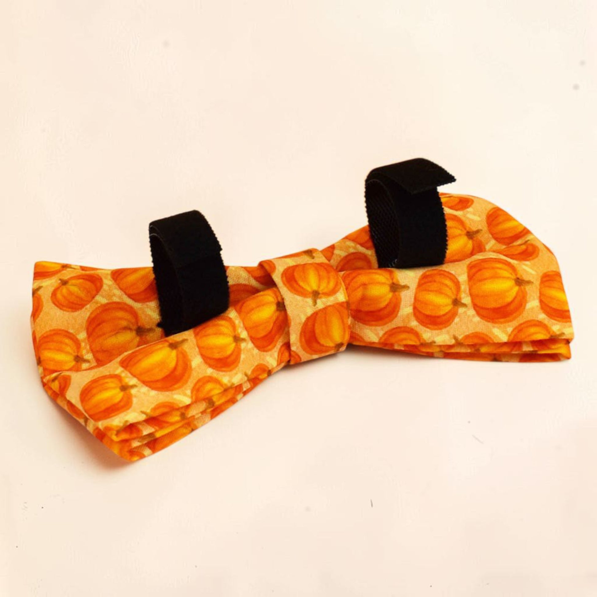 A dog bow tie featuring an all-over pumpkin pattern in shades of orange and yellow.