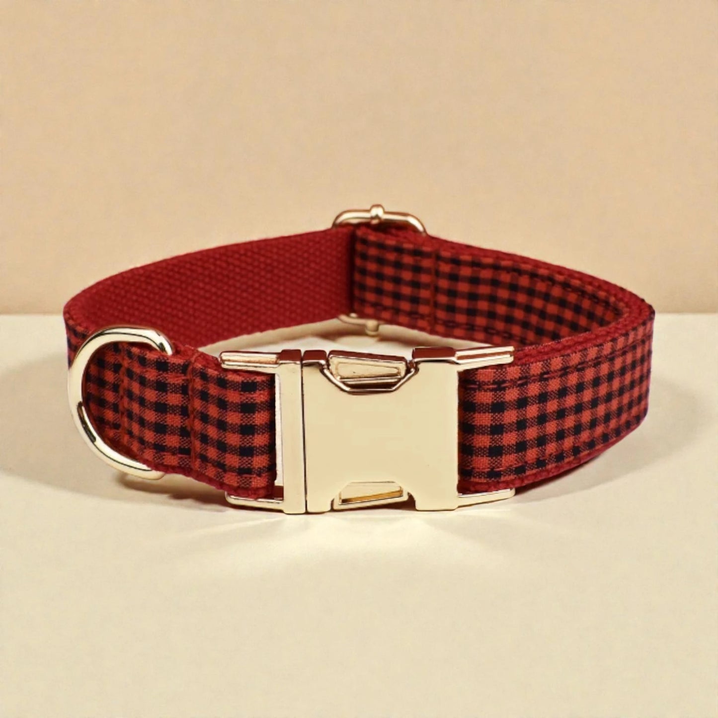 Red and black checkered dog collar with a gold buckle on a beige background