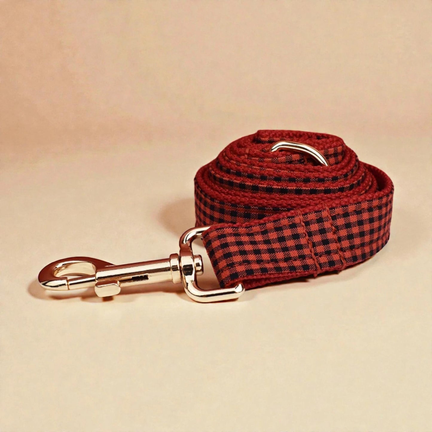 Red and black checkered dog lead with gold clasp on beige background