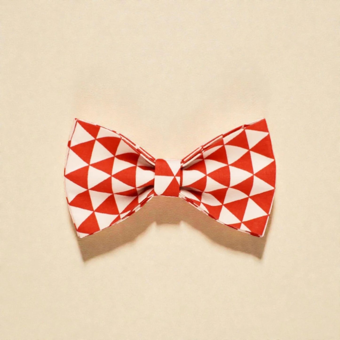 Red and white geometric patterned dog bow tie on a beige background