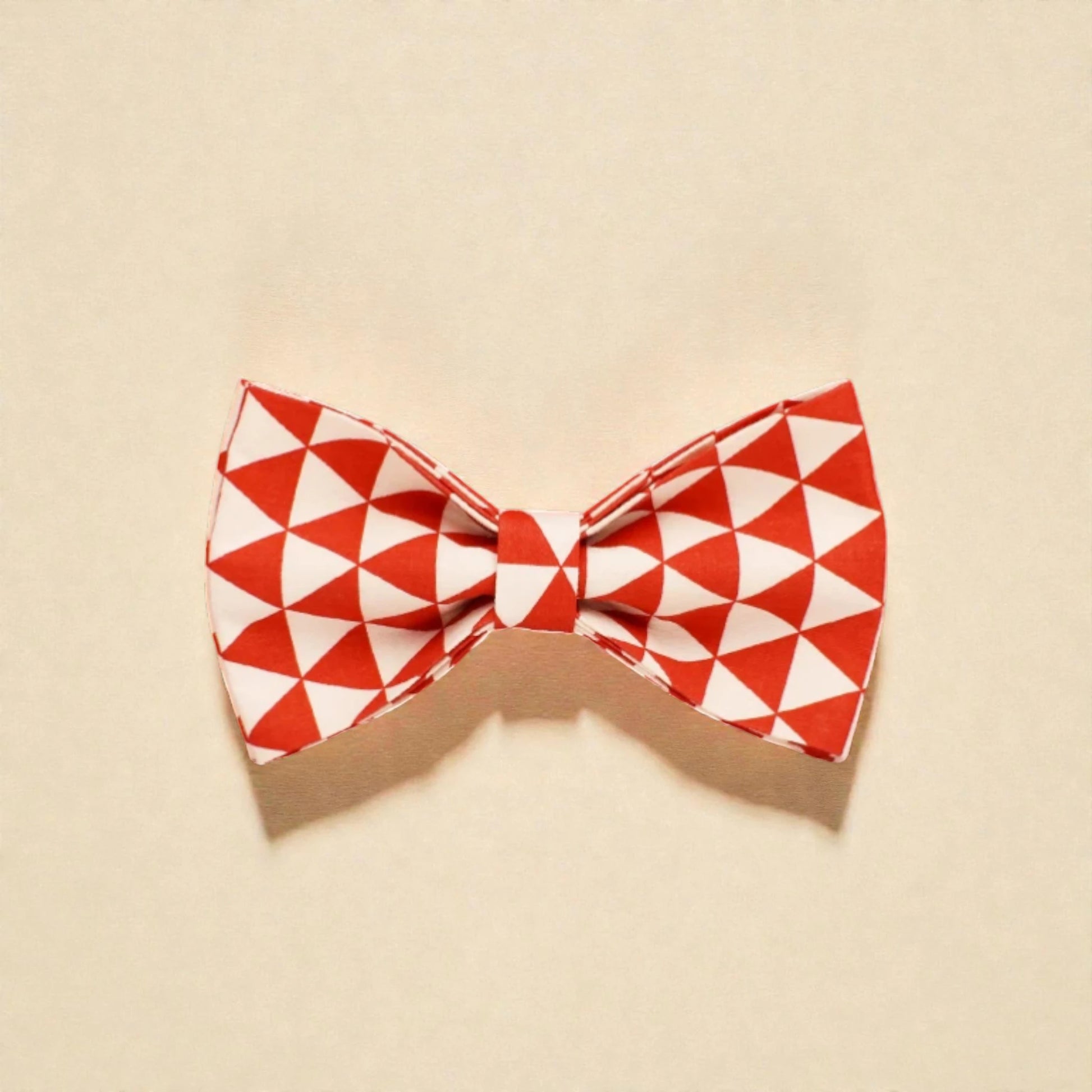 Red and white geometric patterned dog bow tie on a beige background