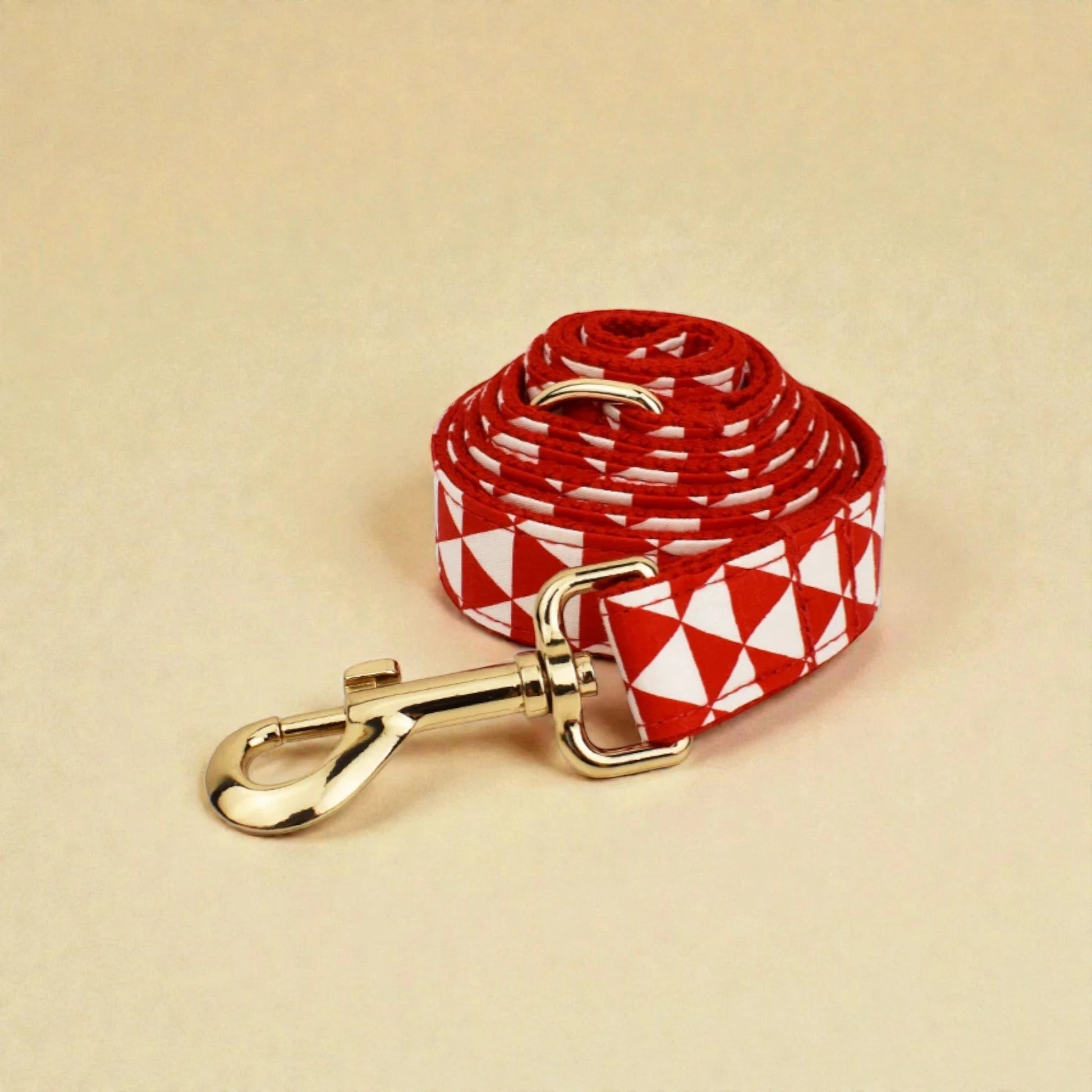 Red and white patterned dog lead with gold clip on beige background