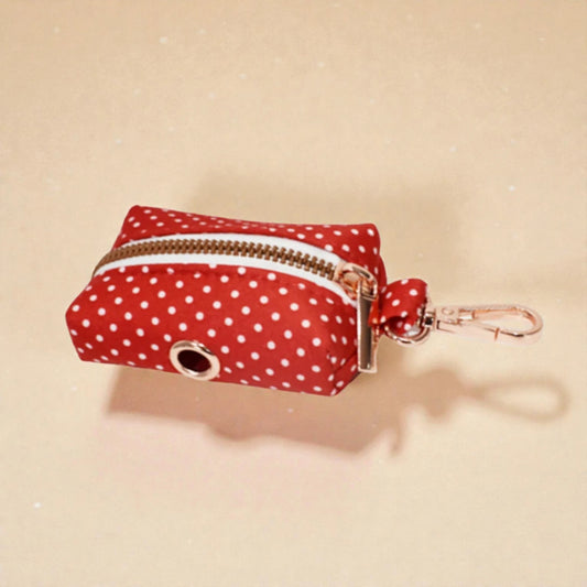 Red polka dot dog poop bag holder with gold zip and clip on beige background