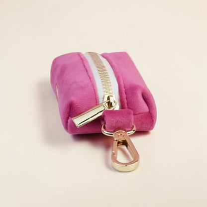 Pink dog poop bag holder with gold zip and clip on a beige background