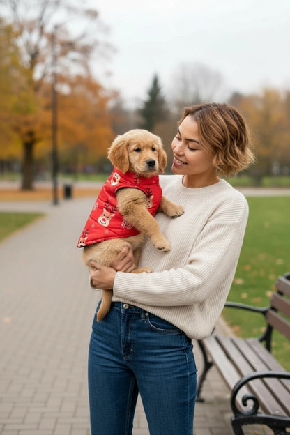 Woman holding a golden puppy wearing a red coat in a park.