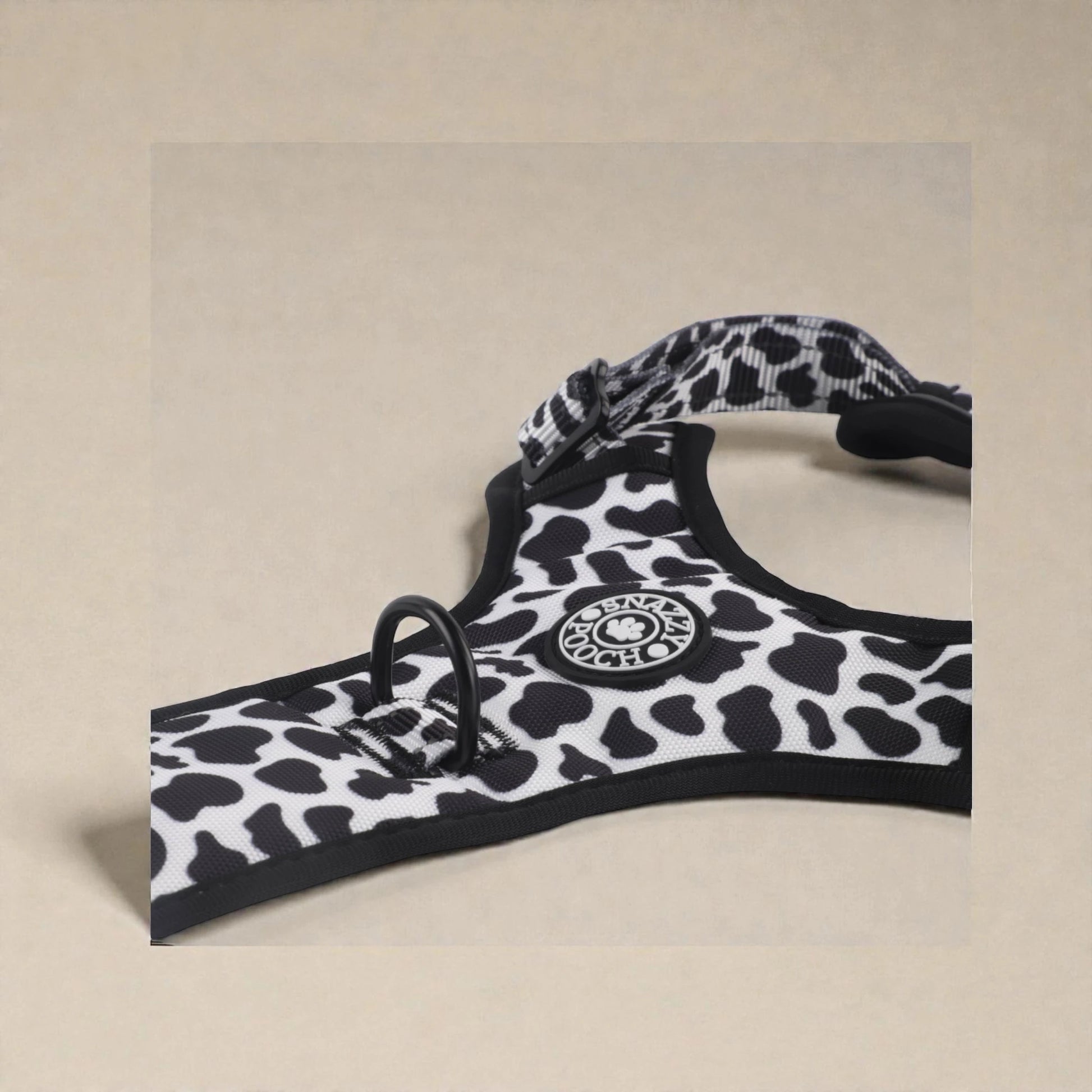 Black and white cow print patterned dog harness on a beige background
